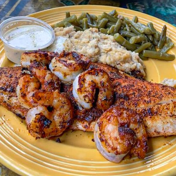 Graham's Landing seafood platter with blackened fish, shrimp, green beans, and grits on a yellow plate.