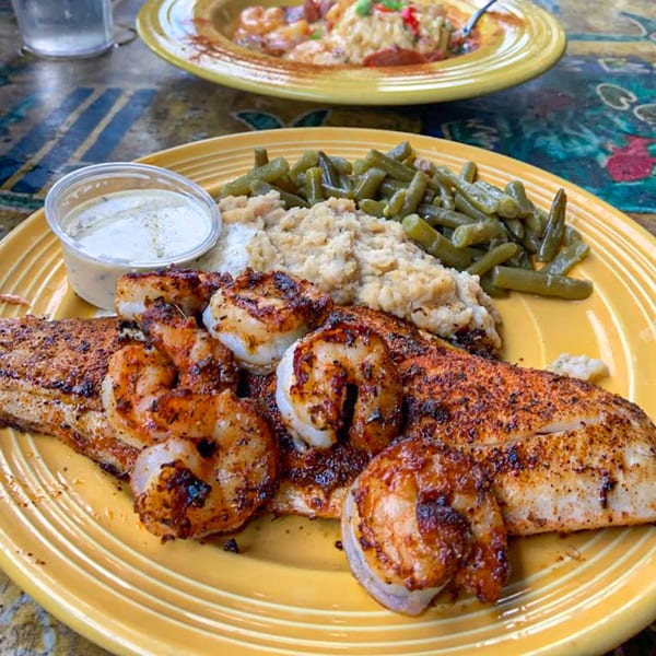 Graham's Landing seafood platter with grilled fish, shrimp, green beans, and grits on a yellow plate.