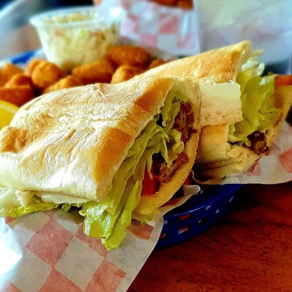 Two large Graham's Landing shrimp po'boy sandwiches with fries and coleslaw in a blue basket.