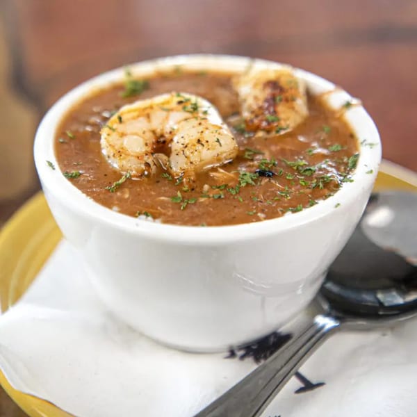 A white bowl of Graham's Landing seafood gumbo with shrimp and parsley, served on a yellow plate.