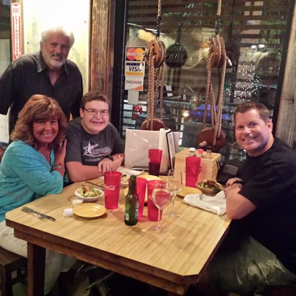 Four smiling people enjoying a meal at a wooden table inside Graham's Landing seafood restaurant.