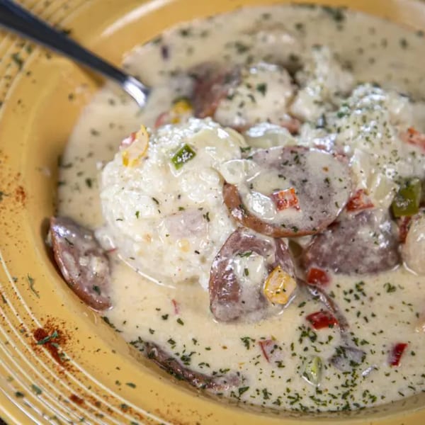 Creamy seafood dish with sausage, potatoes, and vegetables in a yellow bowl with a spoon.