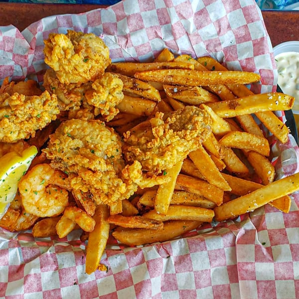 A basket of Graham's Landing fried seafood and french fries with a lemon wedge and tartar sauce.