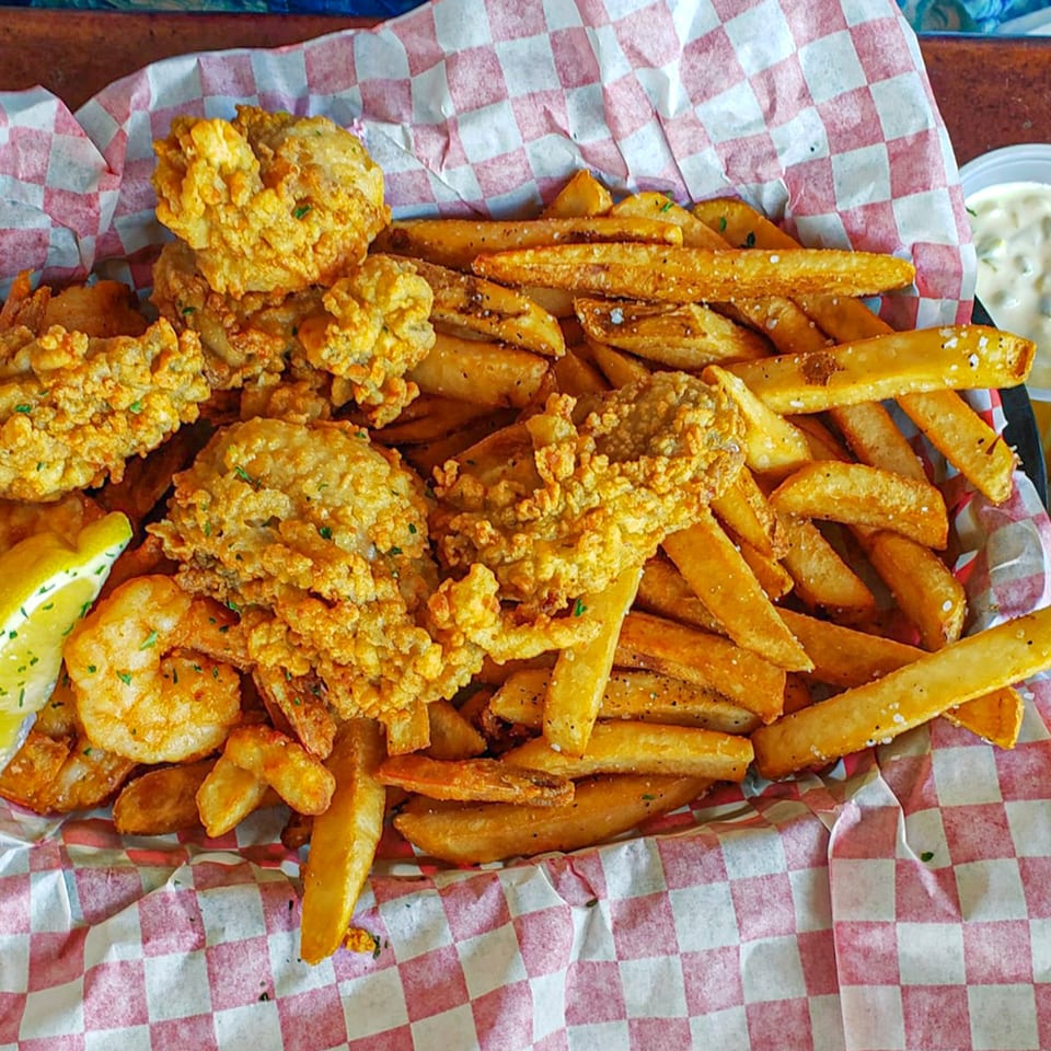 A basket of Graham's Landing fried seafood and french fries with a lemon wedge and tartar sauce.